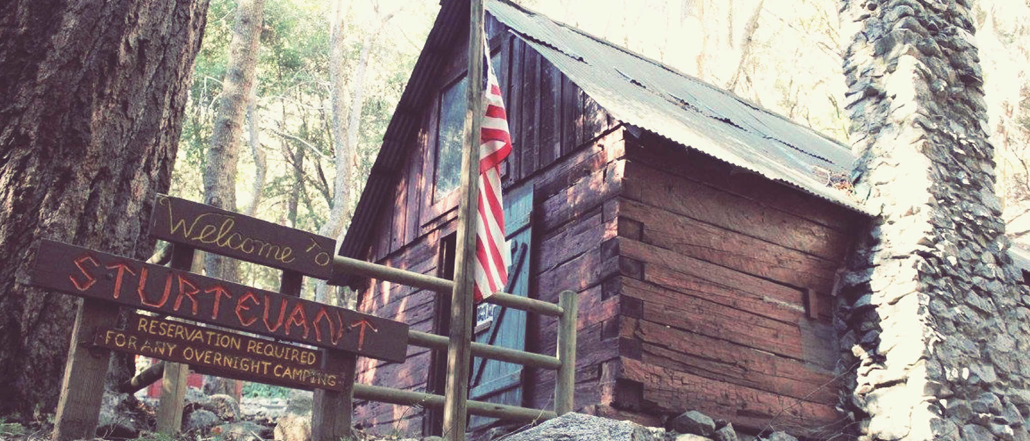 Picture the Sturtevant Camp ranger cabin with U.S. flag and sign welcoming visitors.