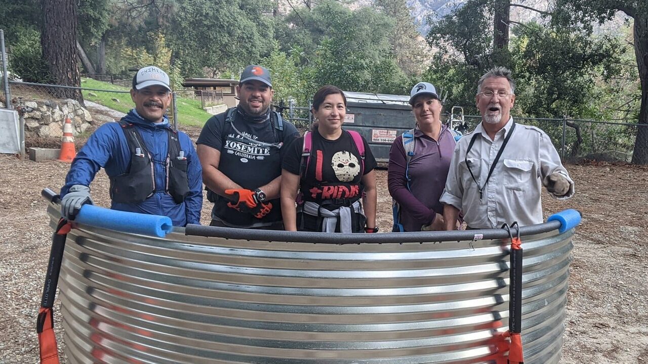 Crew of five posing in front of steel tank part.